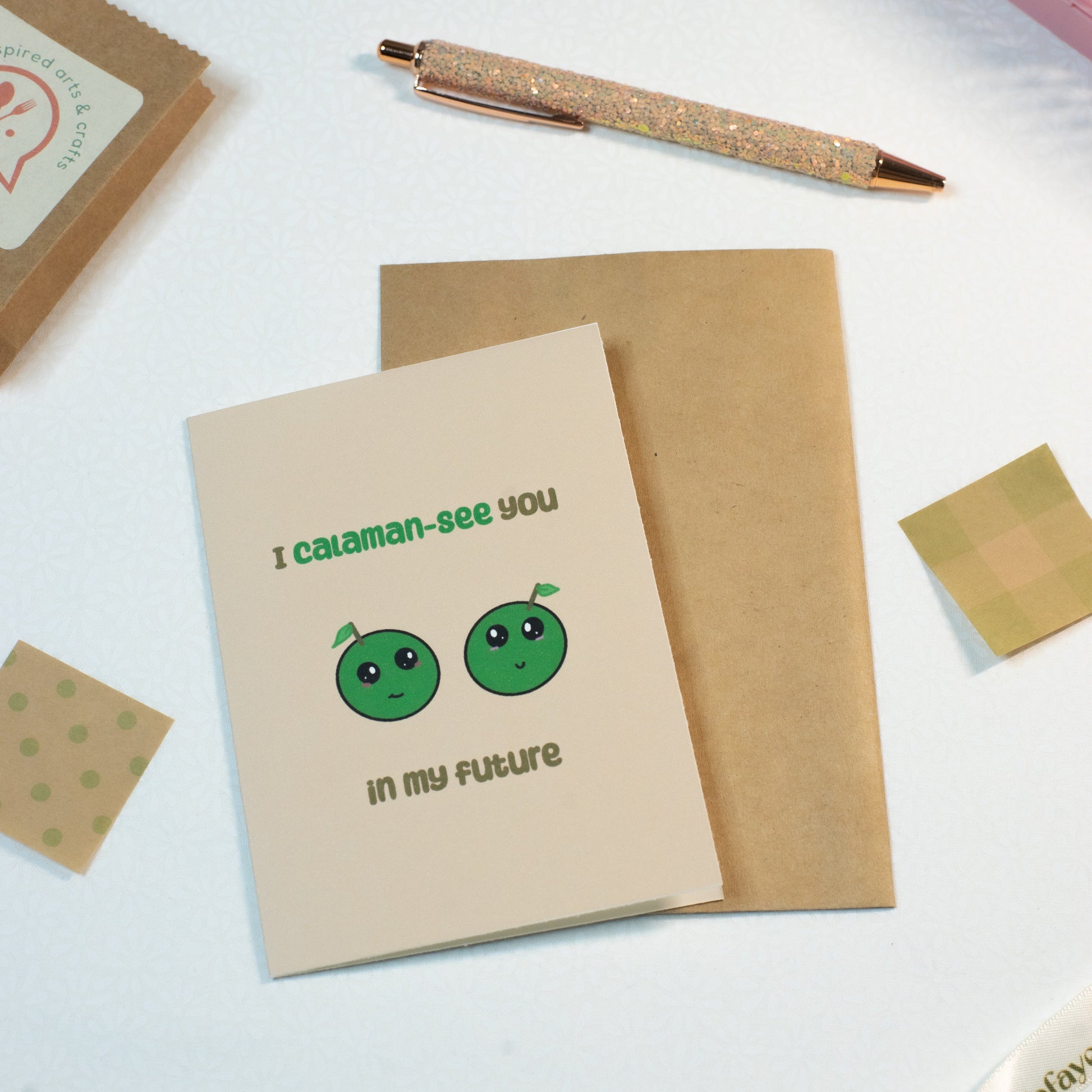 Card with green characters and text on a white surface with stationery items.