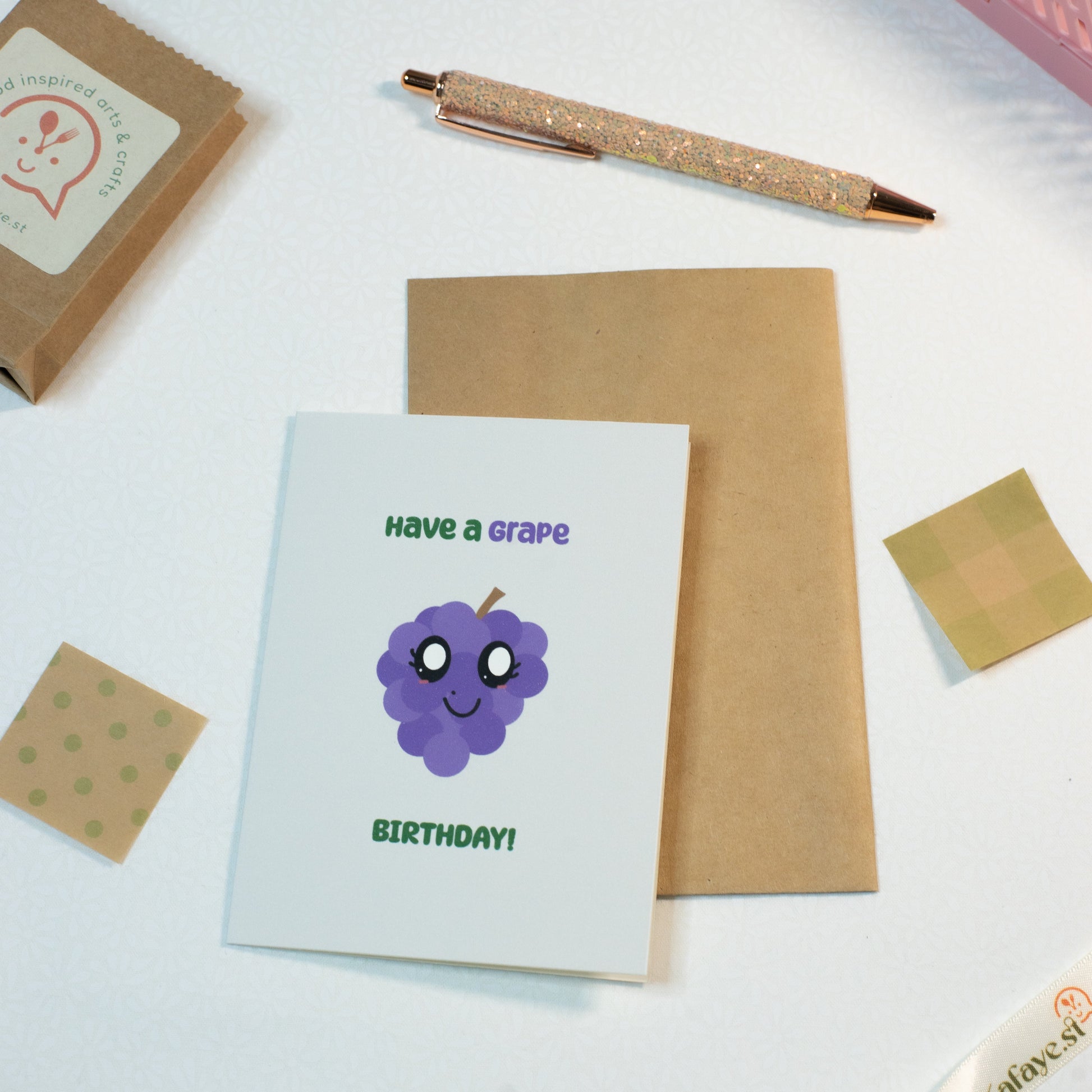 Greeting card with a grape illustration and text on a white surface with stationery items.