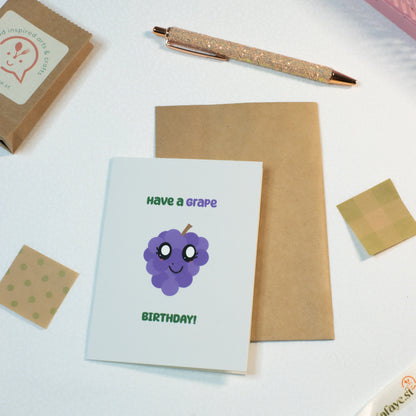 Greeting card with a grape illustration and text on a white surface with stationery items.