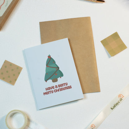 Christmas card with tree design and 'Have a Merry Christmas' text on a white surface with stationery items.